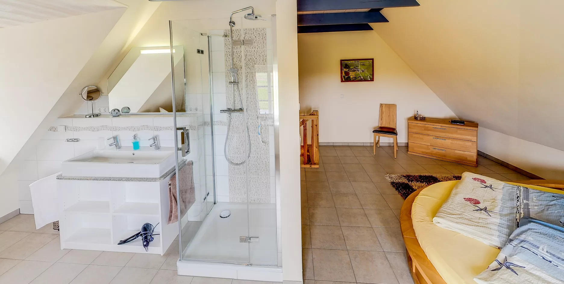 Dachzimmer mit integriertem Bad, Dusche links und gemütlichem Sitzbereich rechts.