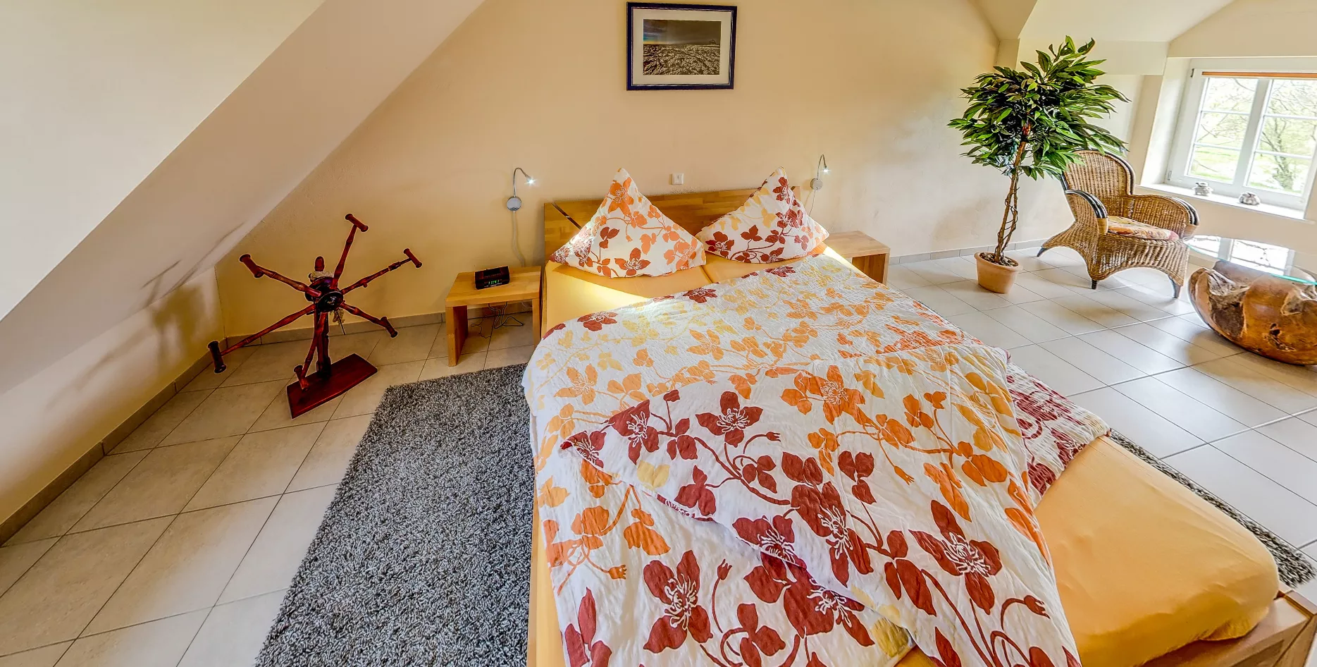 Schlafzimmer mit Doppelbett und floraler Bettwäsche unter Dachschräge