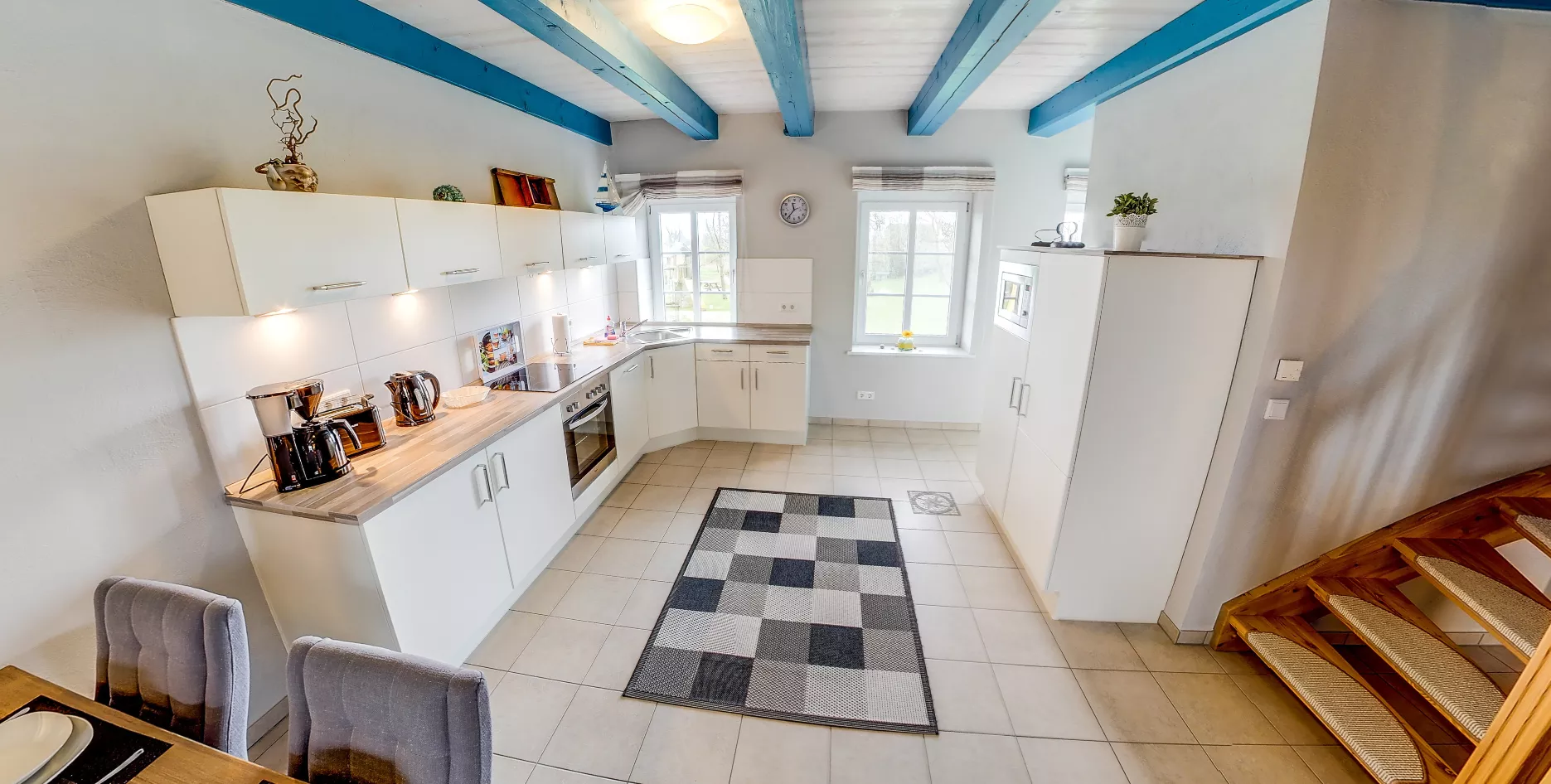 Küche Seegarden – weiße Fronten, blaue Balken und Wanduhr zwischen zwei Fenstern