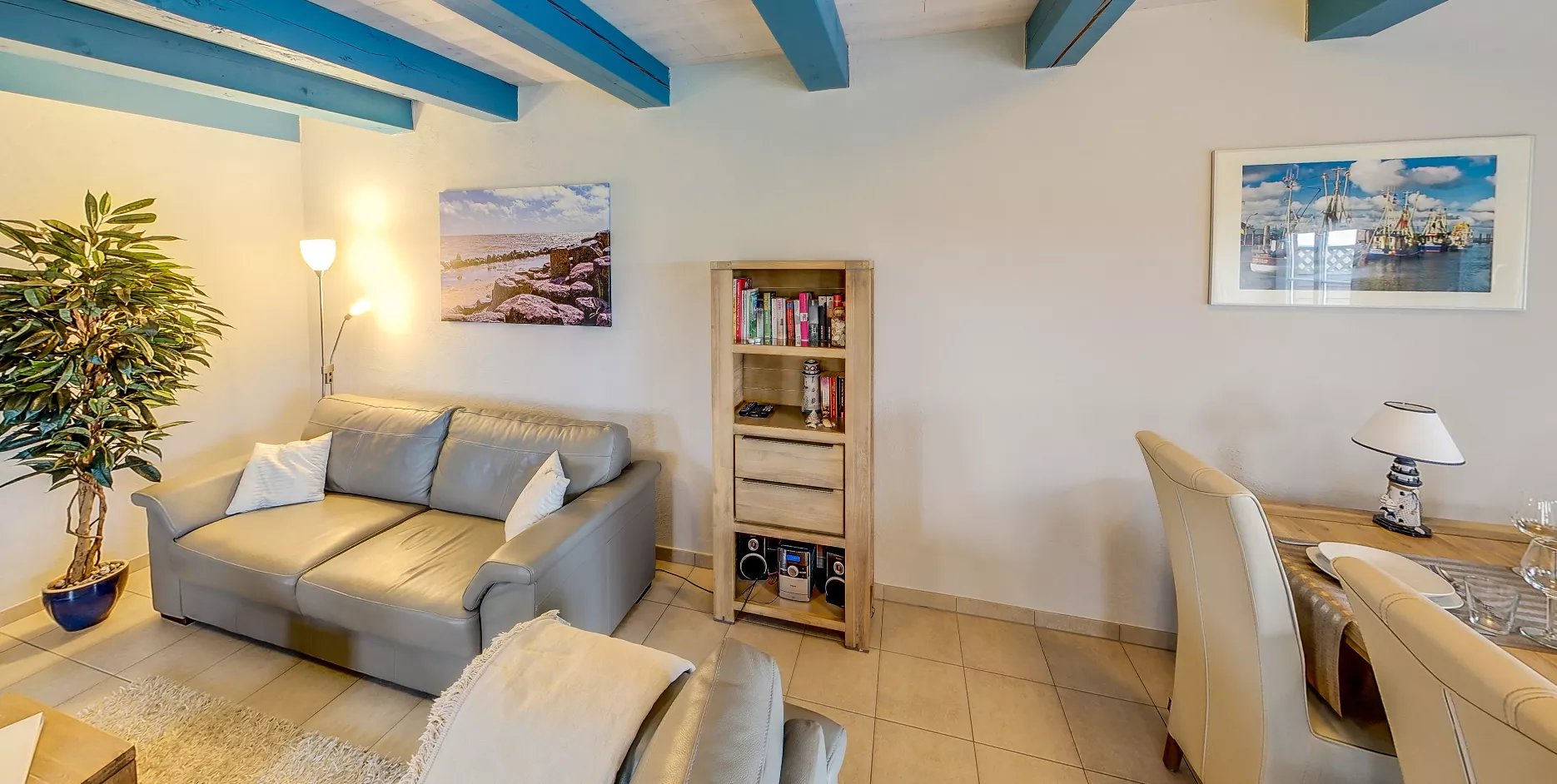 Wohnbereich mit grauem Ledersofa, Esstisch und blauen Deckenbalken