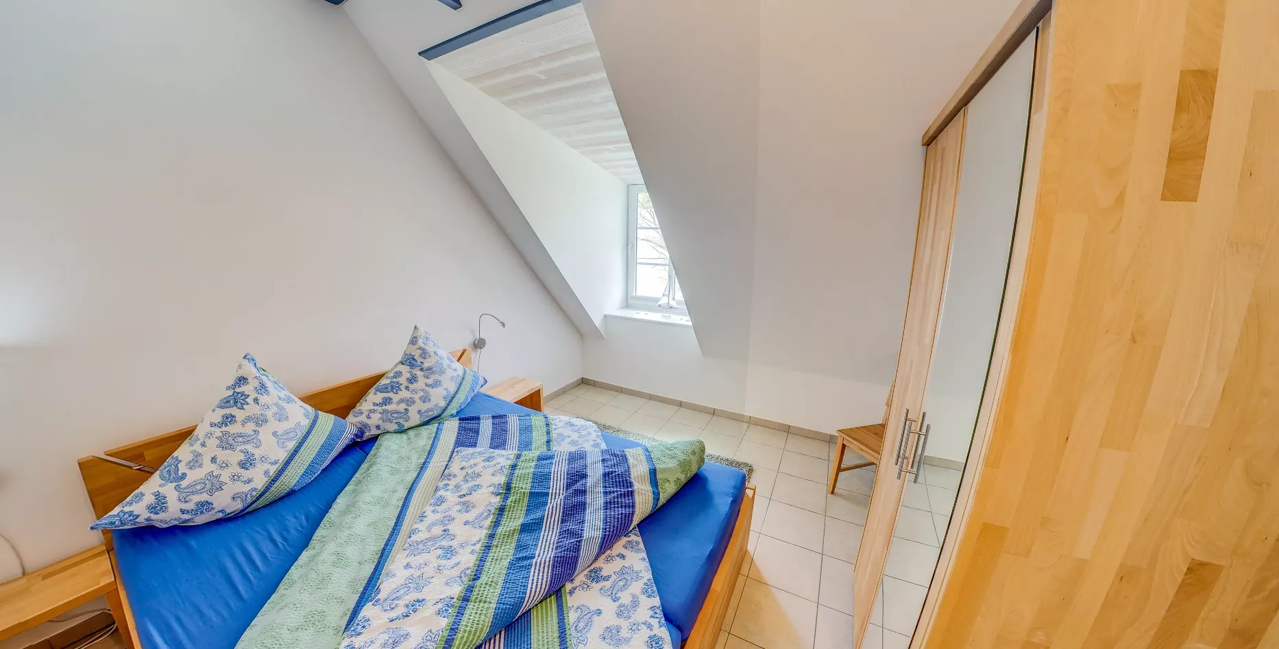 Schlafzimmer mit Doppelbett und blau-grüner Bettwäsche unter Dachschräge