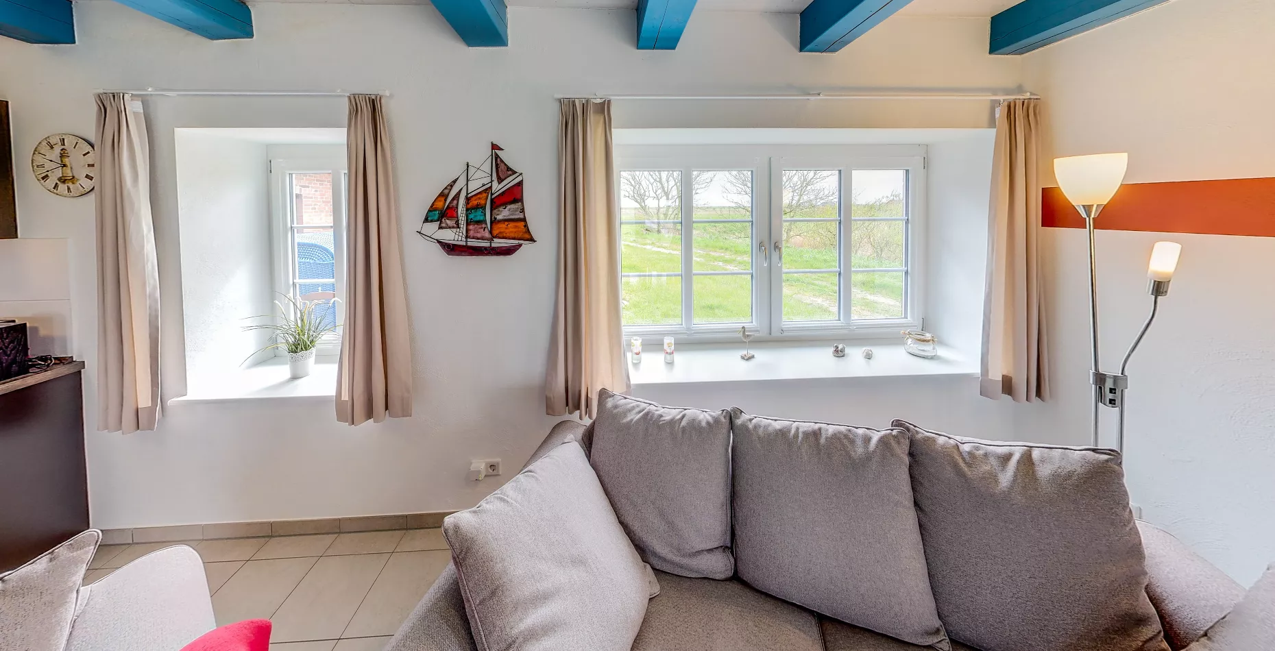 Fensterplatz Leuchtturm – graues Sofa, Segelboot-Deko und Blick ins Grüne