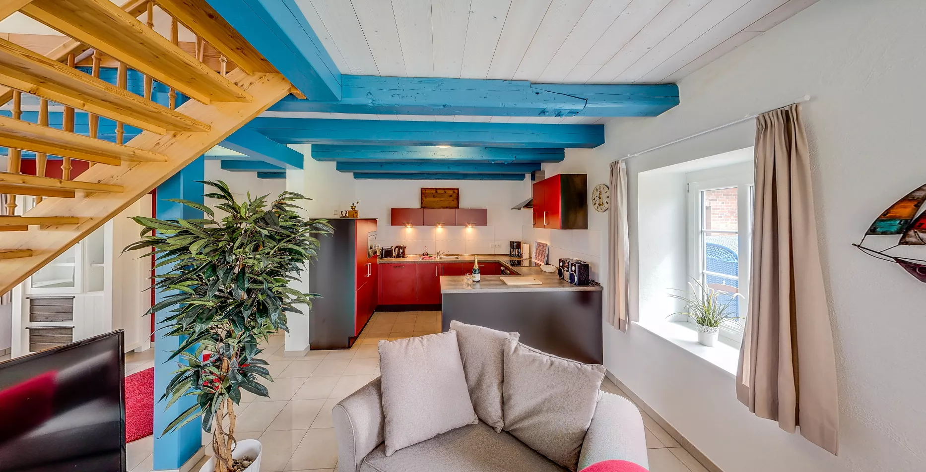 Küche der Ferienwohnung Leuchtturm – rote Fronten, blaue Balken und Holztreppe
